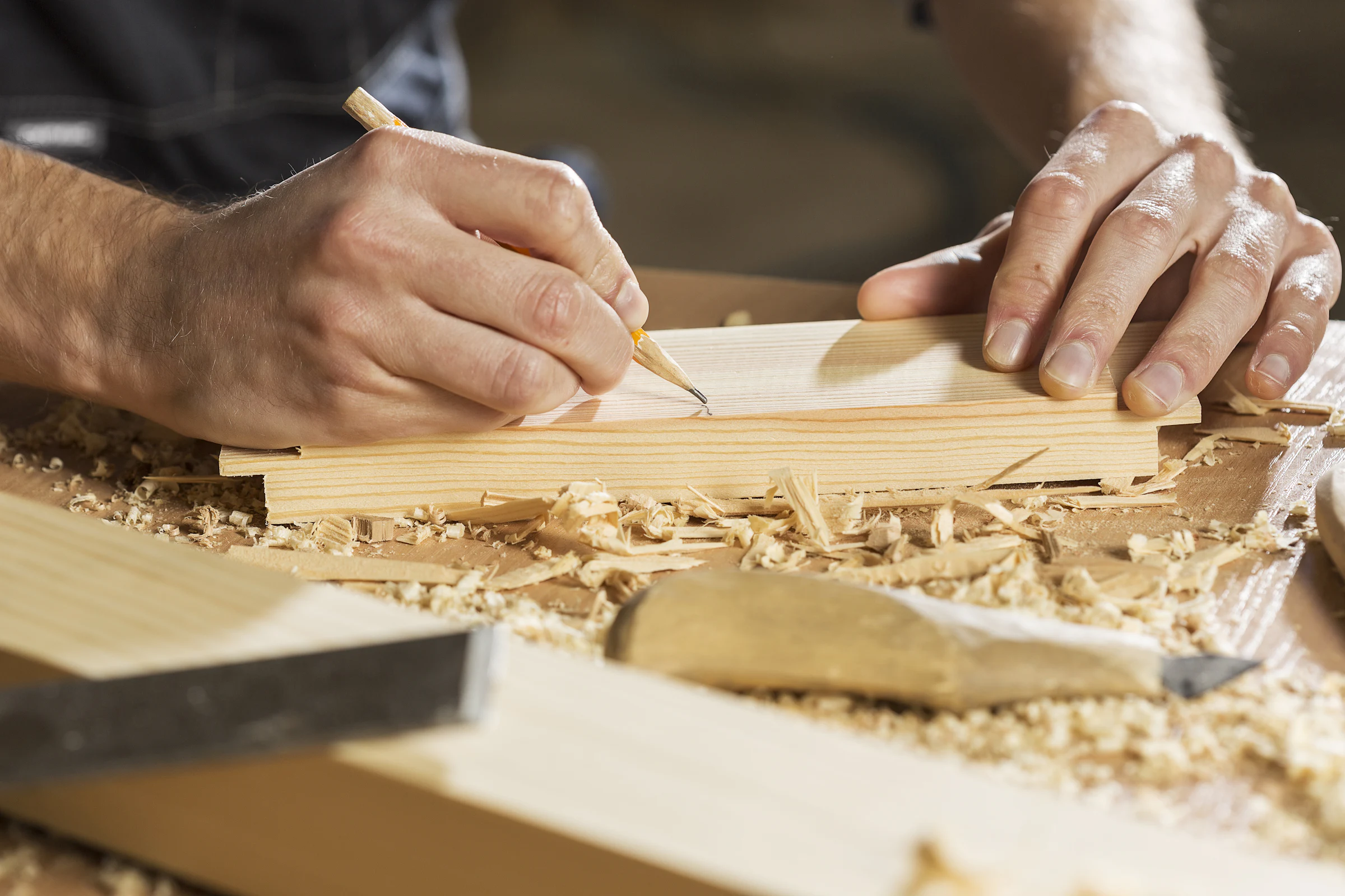 Hände reißen mit Bleistift und Winkel eine Linie auf einem Holzbrett an