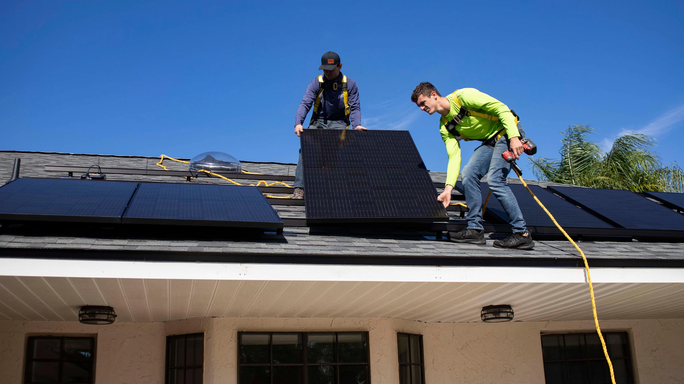 Zwei Monteure tragen ein Solarmodul über ein Hausdach